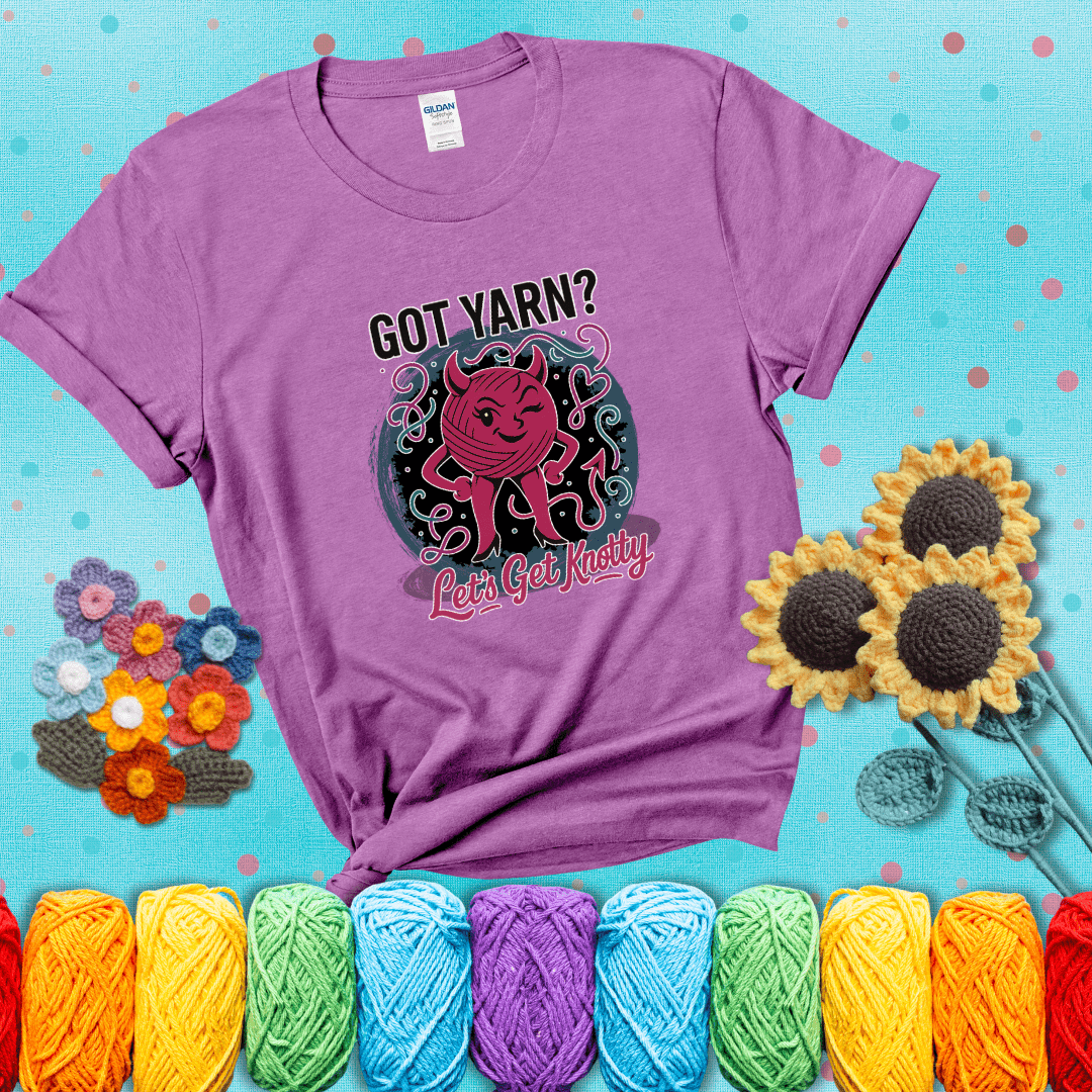 A cheeky pink yarn ball with devil horns, arms, and legs winks under the text “Got Yarn? Let’s Get Knotty,” showing a light purple tee with a teal sunflower background