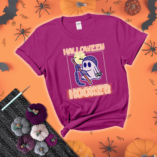 Cartoon ghost crocheter with a yarn ball head, crochet hook, bats, and text “Halloween Hooker,” a fun spooky tee for yarn lovers showing a magenta tee with a festive Halloween background