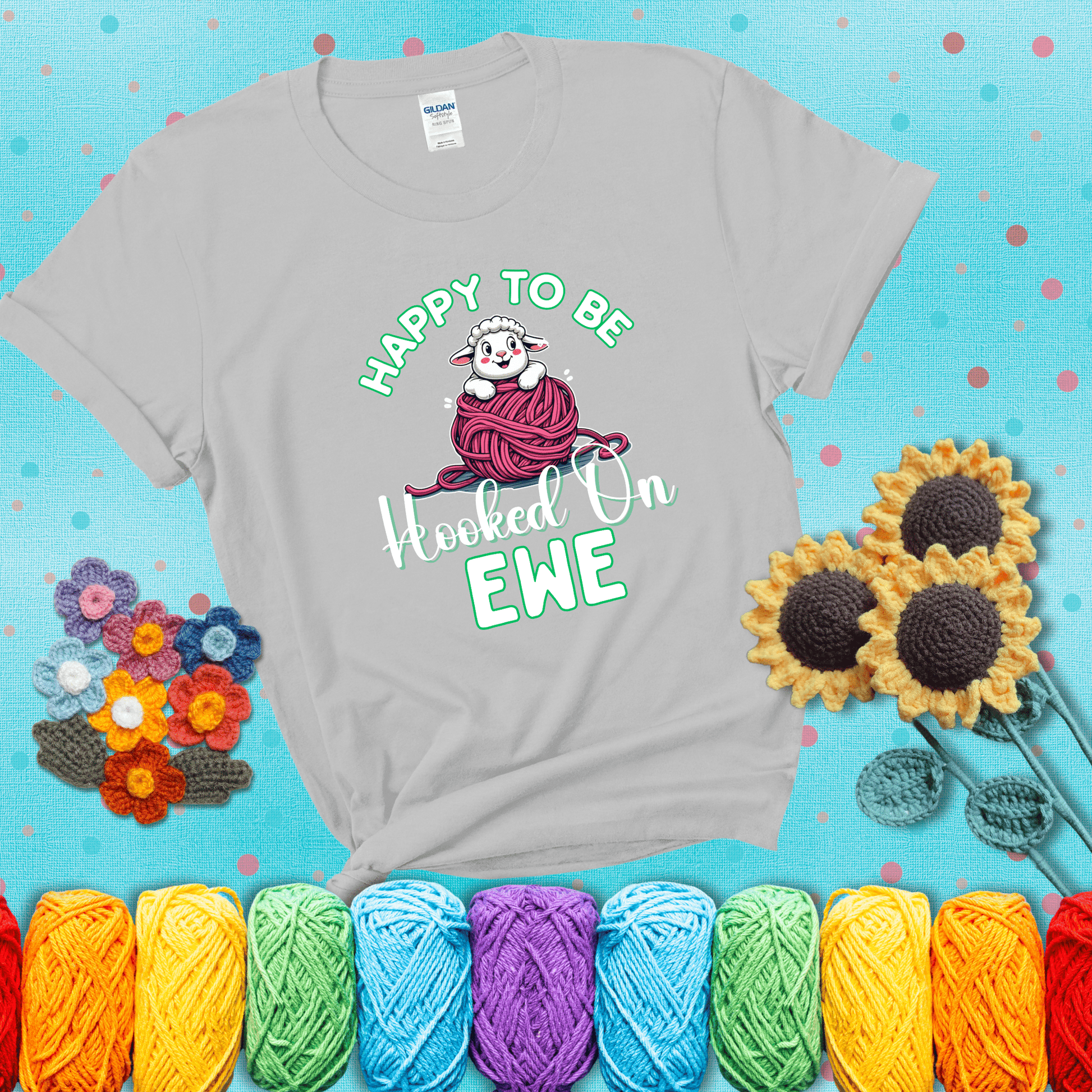 Smiling cartoon sheep peeks from a pink yarn ball, surrounded by green text “Happy to Be Hooked on Ewe” — playful and affectionate sheep pun for crocheters showing a light grey tee with a teal sunflower background