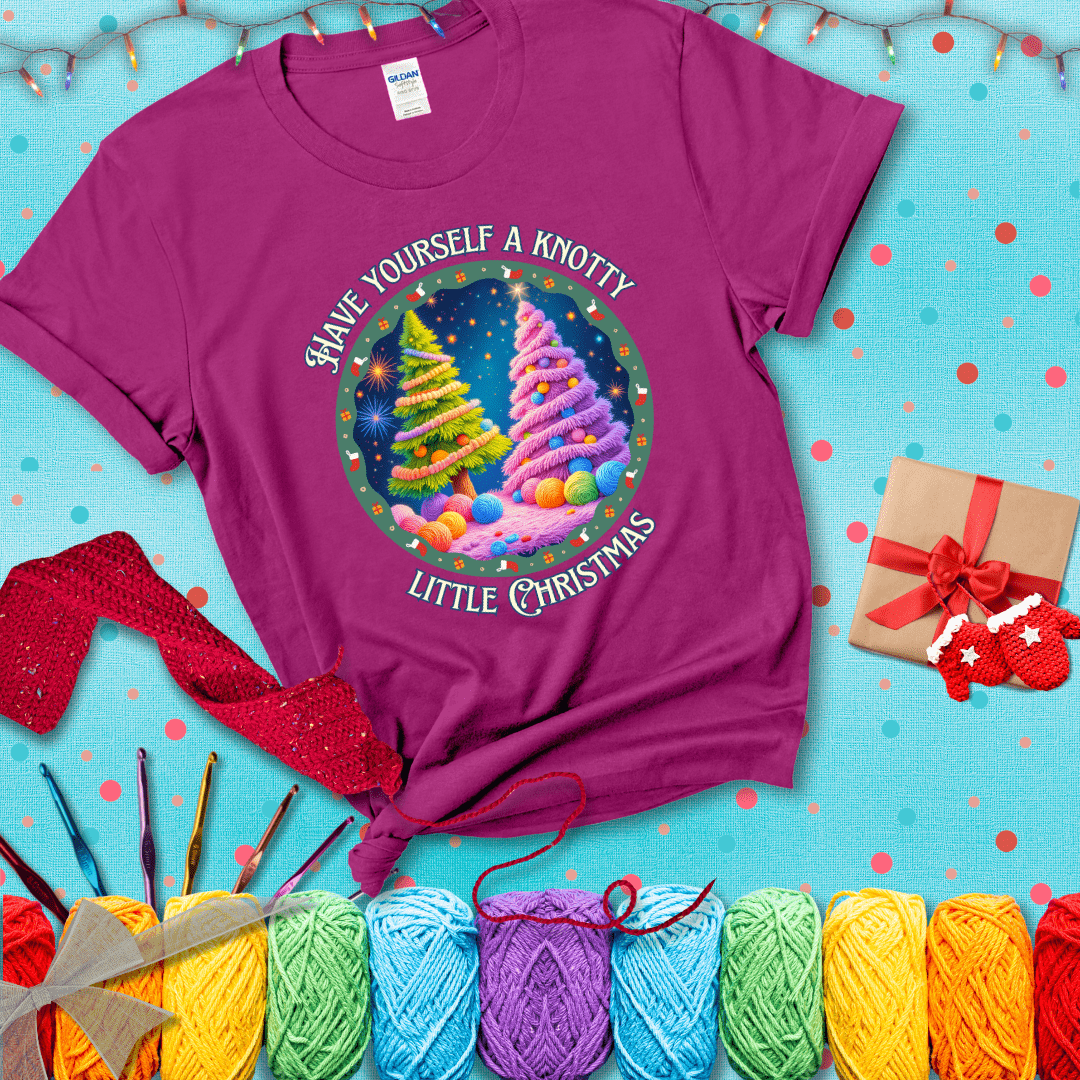 Two yarn-covered Christmas trees wrapped in colorful strands of yarn, with the phrase "Have Yourself a Knotty Little Christmas" encircling the scene showing a magenta tee with a festive Christmas background