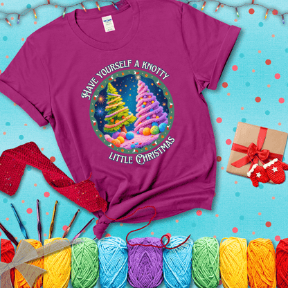 Two yarn-covered Christmas trees wrapped in colorful strands of yarn, with the phrase "Have Yourself a Knotty Little Christmas" encircling the scene showing a magenta tee with a festive Christmas background