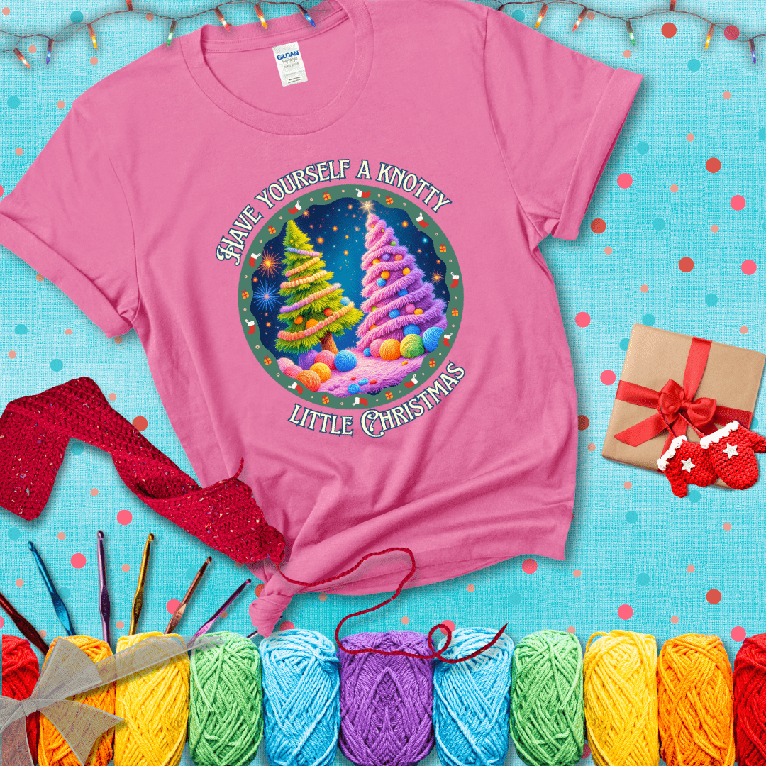 Two yarn-covered Christmas trees wrapped in colorful strands of yarn, with the phrase "Have Yourself a Knotty Little Christmas" encircling the scene showing a pink tee with a festive Christmas background