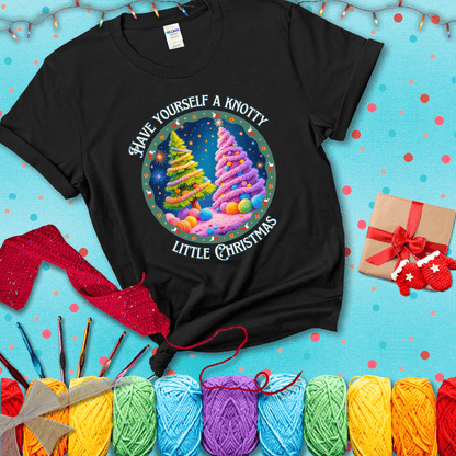 Two yarn-covered Christmas trees wrapped in colorful strands of yarn, with the phrase "Have Yourself a Knotty Little Christmas" encircling the scene showing a black tee with a festive Christmas background