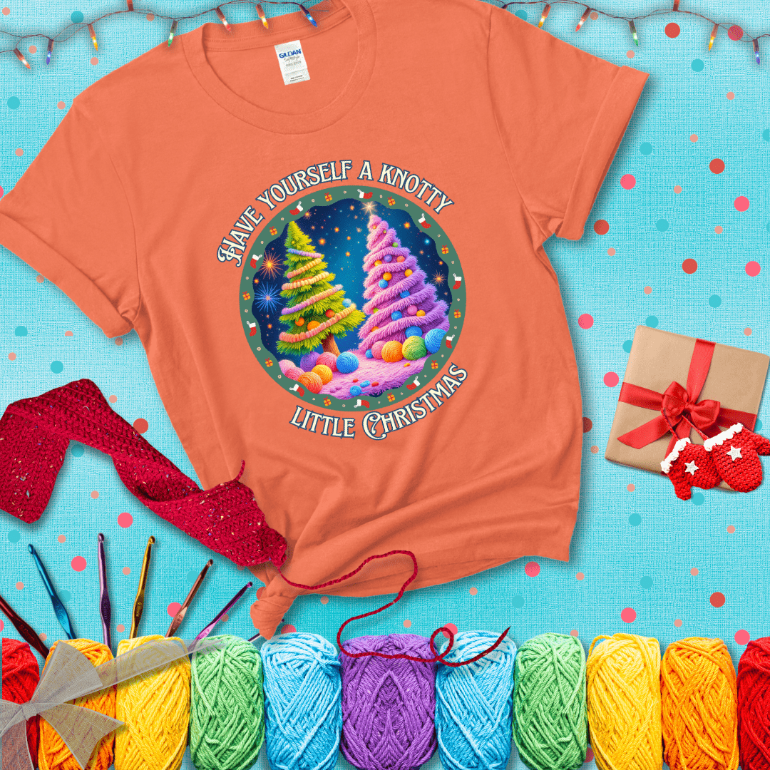 Two yarn-covered Christmas trees wrapped in colorful strands of yarn, with the phrase "Have Yourself a Knotty Little Christmas" encircling the scene showing a light orange tee with a festive Christmas background
