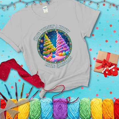Two yarn-covered Christmas trees wrapped in colorful strands of yarn, with the phrase "Have Yourself a Knotty Little Christmas" encircling the scene showing a light grey tee with a festive Christmas background