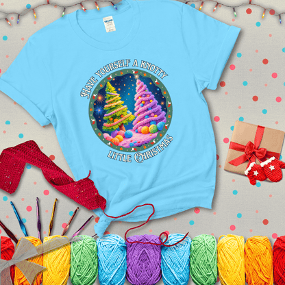 Two yarn-covered Christmas trees wrapped in colorful strands of yarn, with the phrase "Have Yourself a Knotty Little Christmas" encircling the scene showing a light blue tee with a festive Christmas background