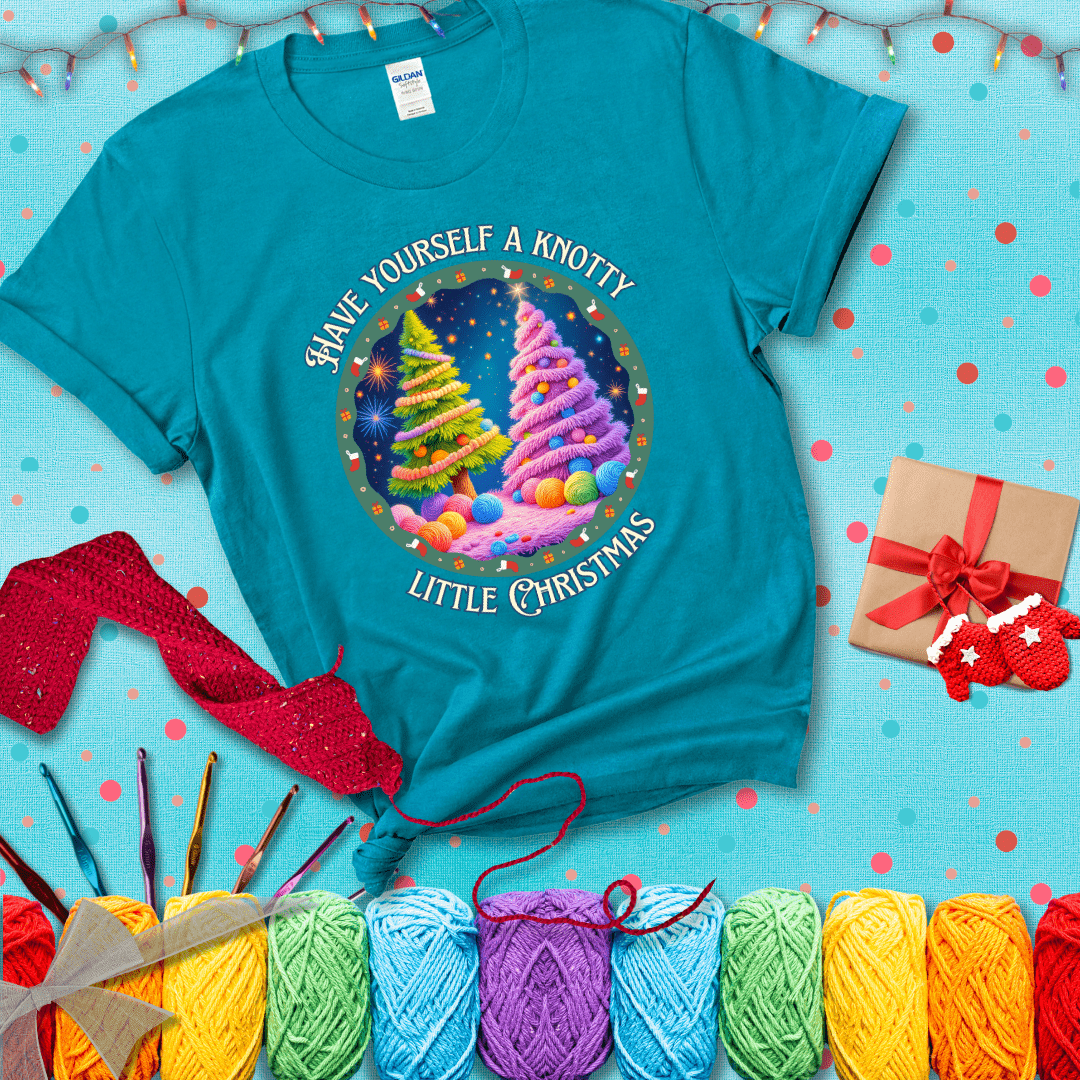 Two yarn-covered Christmas trees wrapped in colorful strands of yarn, with the phrase "Have Yourself a Knotty Little Christmas" encircling the scene showing a blue-green tee with a festive Christmas background
