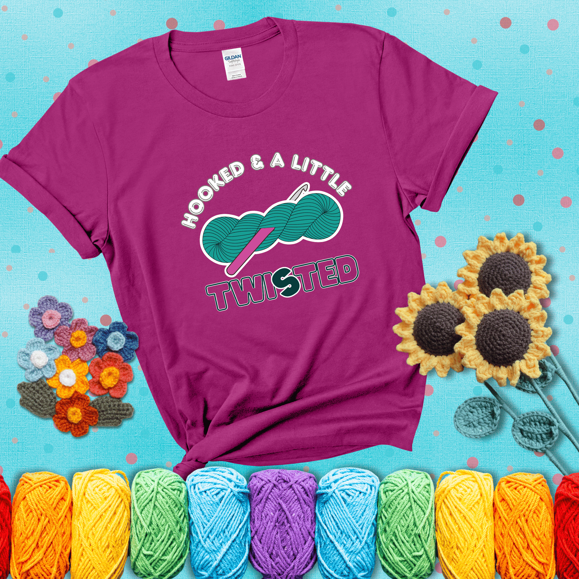 A teal skein of yarn with a hot pink crochet hook through it, captioned “Hooked & a Little Twisted” showing a magenta tee with a teal sunflower background