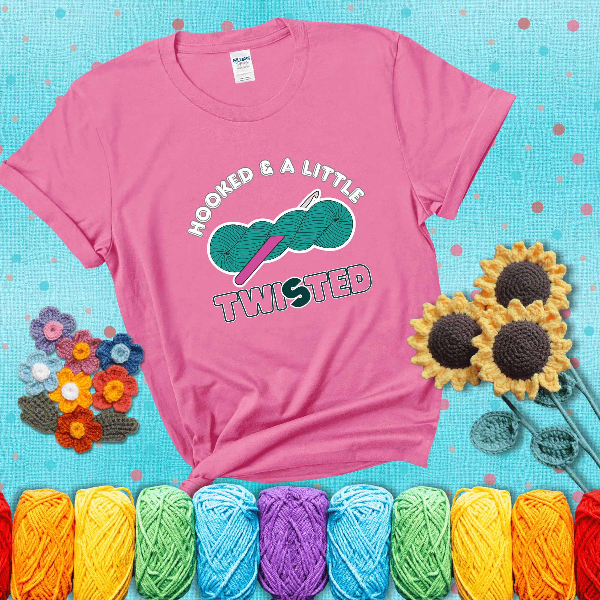 A teal skein of yarn with a hot pink crochet hook through it, captioned “Hooked & a Little Twisted” showing a pink tee with a teal sunflower background