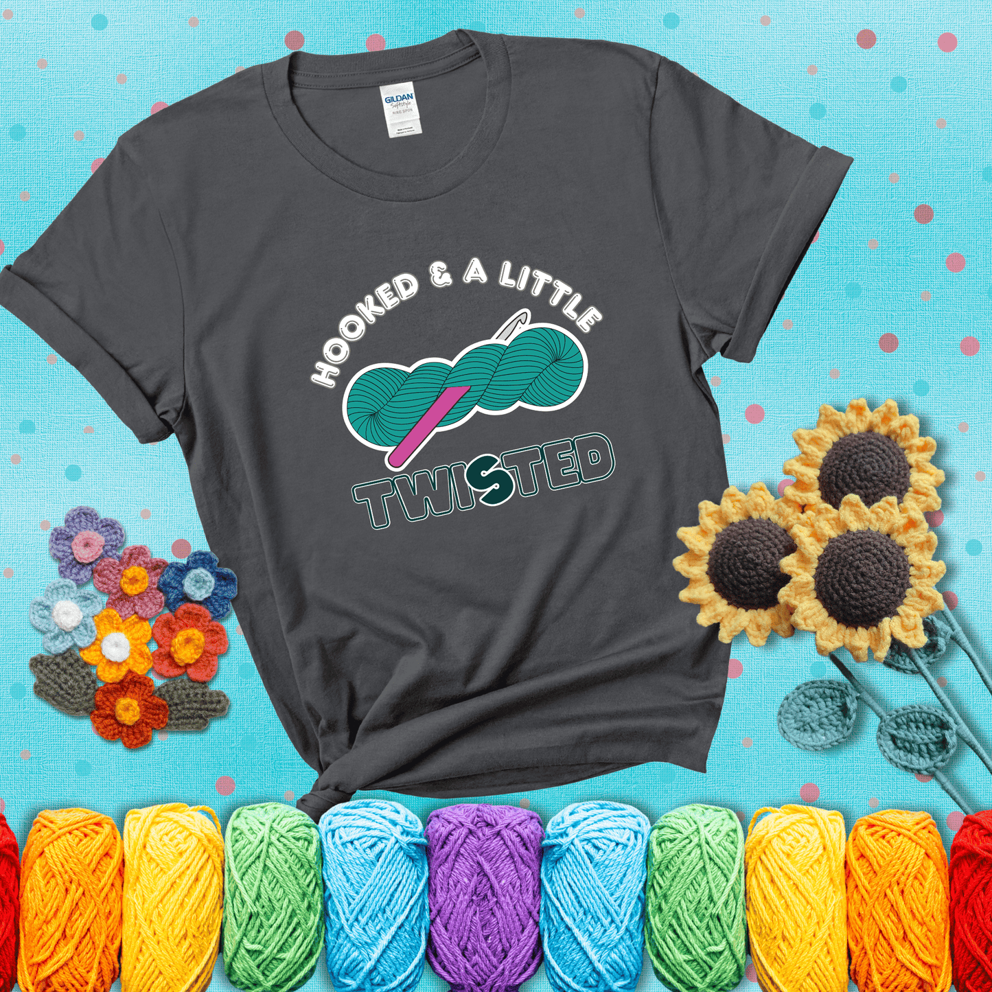 A teal skein of yarn with a hot pink crochet hook through it, captioned “Hooked & a Little Twisted” showing a dark grey tee with a teal sunflower background