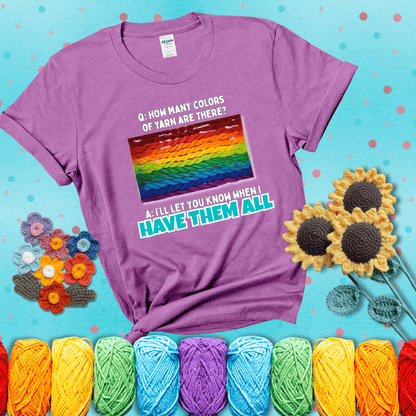 Rainbow skeins of yarn stacked in color gradient with playful question: “How many colors of yarn are there?” Answer: “I'll let you know when I have them all” showing a light purple tee with a teal sunflower background