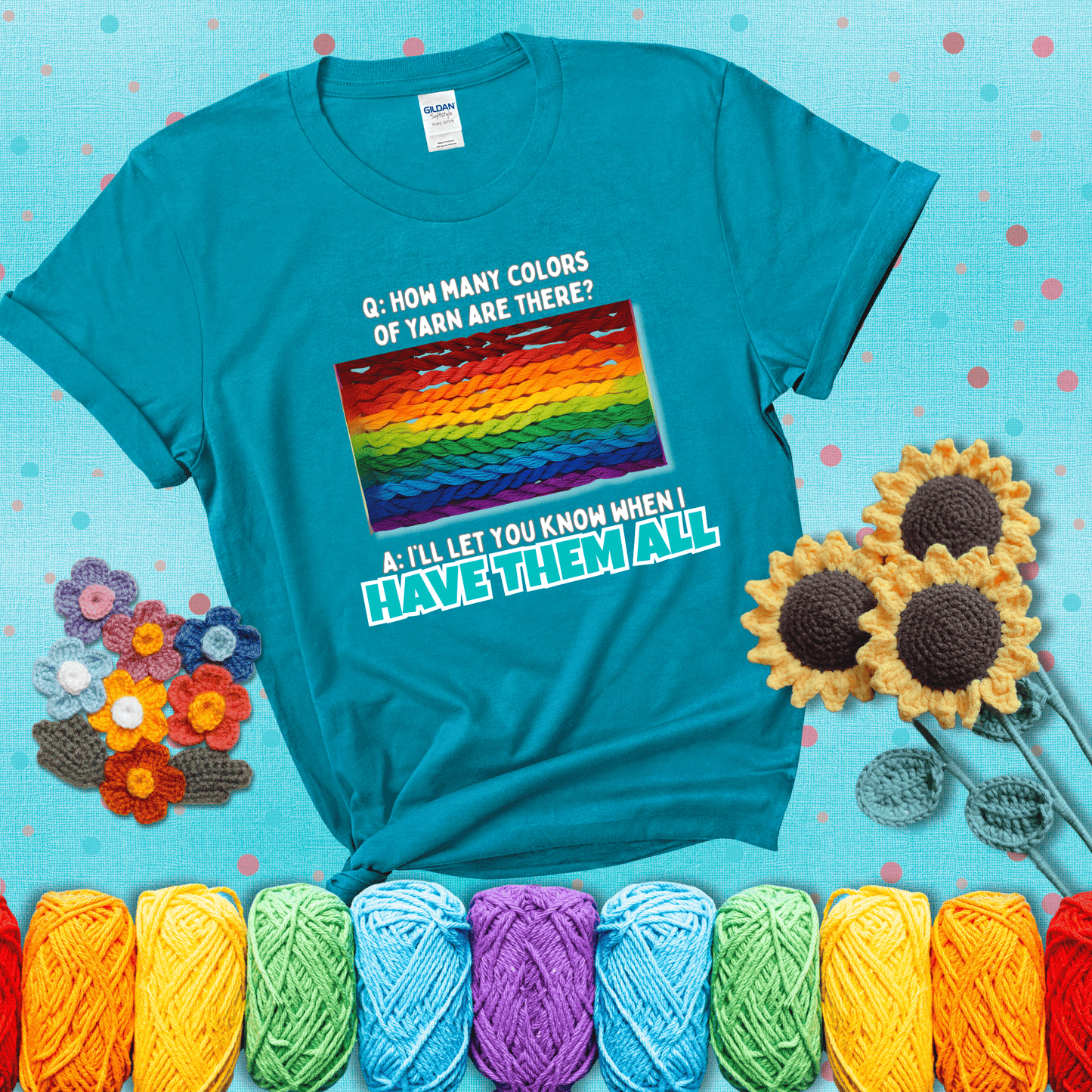 Rainbow skeins of yarn stacked in color gradient with playful question: “How many colors of yarn are there?” Answer: “I'll let you know when I have them all” showing a blue-green tee with a teal sunflower background