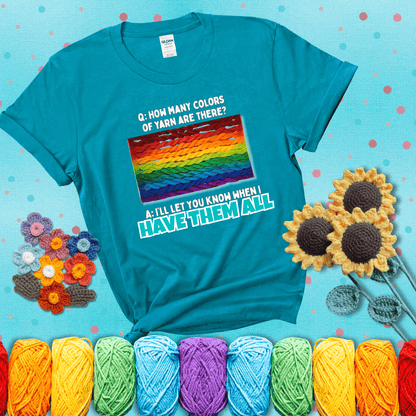 Rainbow skeins of yarn stacked in color gradient with playful question: “How many colors of yarn are there?” Answer: “I'll let you know when I have them all” showing a blue-green tee with a teal sunflower background