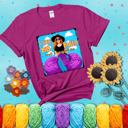 Bold cartoon image of a woman crocheting between two giant purple yarn balls with the phrase “I like big balls and I cannot lie” in retro fonts showing a magenta tee with a teal sunflower background