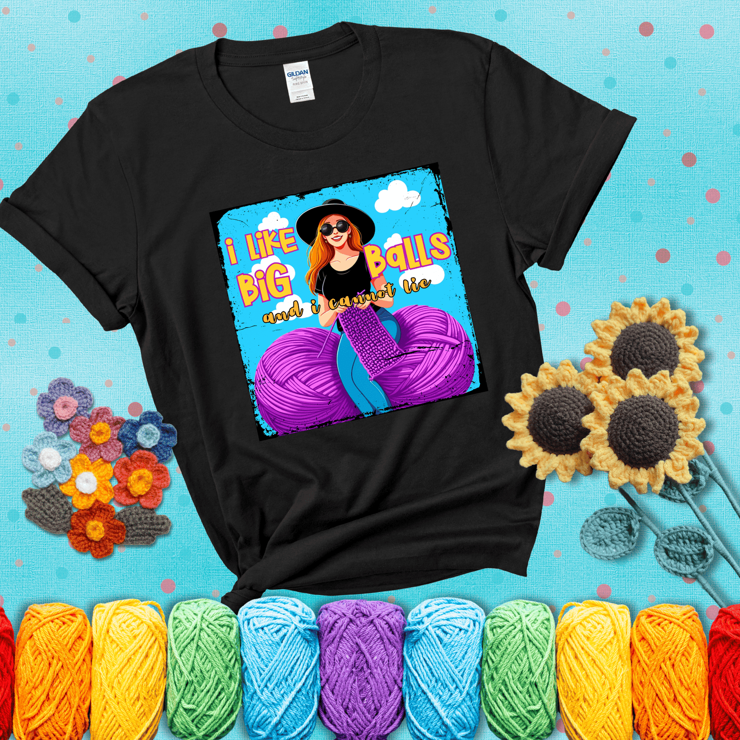 Bold cartoon image of a woman crocheting between two giant purple yarn balls with the phrase “I like big balls and I cannot lie” in retro fonts showing a black tee with a teal sunflower background