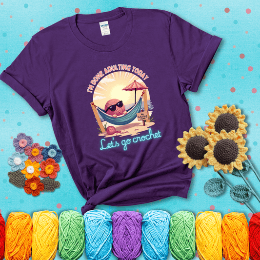 A chill yarn ball wearing sunglasses lounges in a hammock on a beach under the sun with the phrase “I’m done adulting today – Let’s go crochet,” showing a purple tee with a teal sunflower background