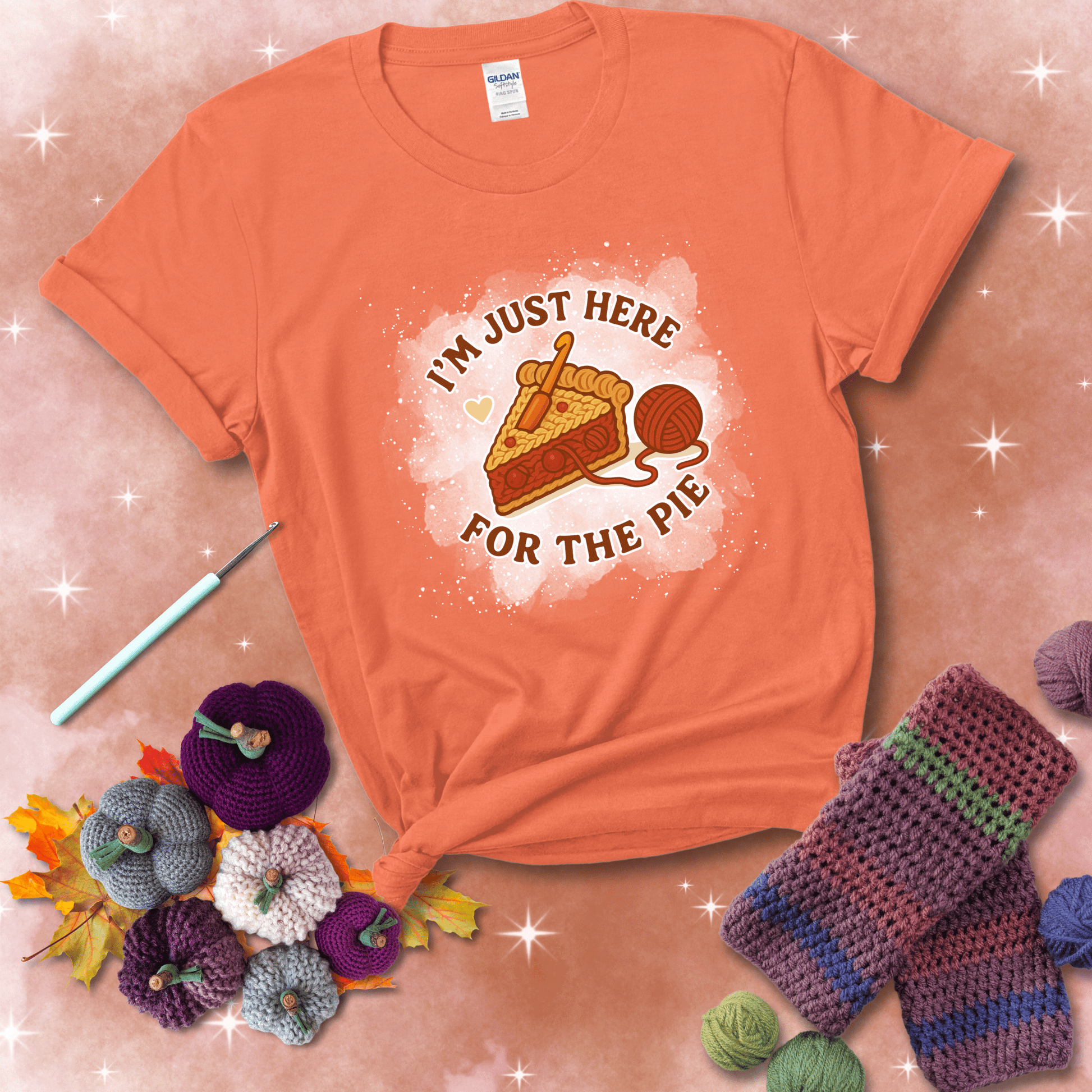 A slice of cherry pie with a crochet hook tucked in the filling and yarn trailing out, blending baking with crochet fun, showing a light orange tee with a festive Fall background