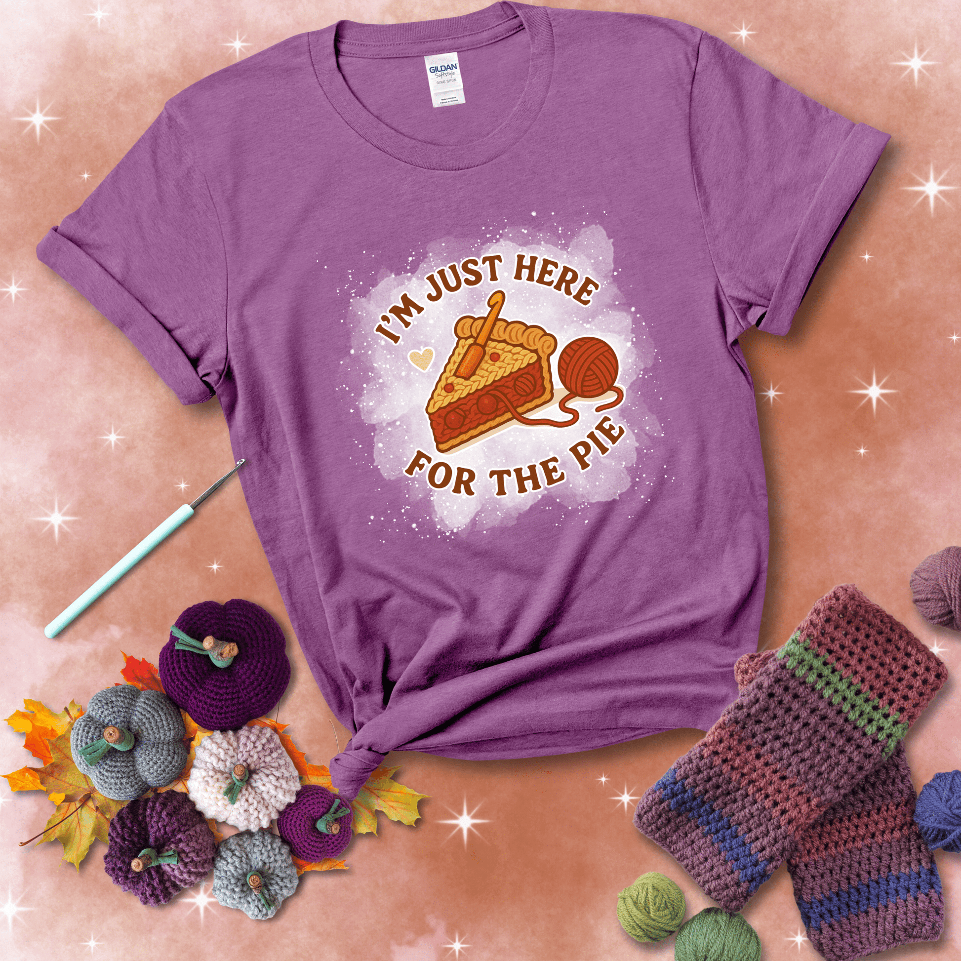 A slice of cherry pie with a crochet hook tucked in the filling and yarn trailing out, blending baking with crochet fun, showing a light purple tee with a festive Fall background
