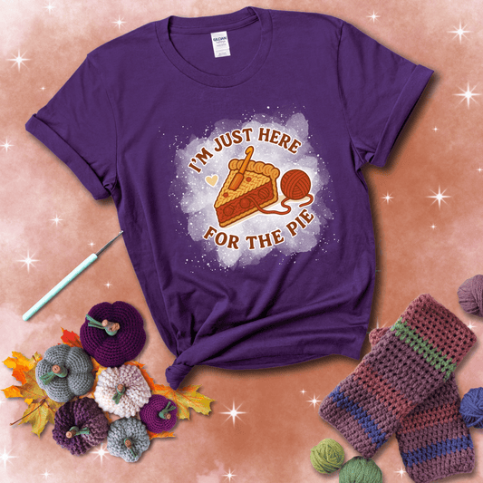 A slice of cherry pie with a crochet hook tucked in the filling and yarn trailing out, blending baking with crochet fun, showing a purple tee with a festive Fall background