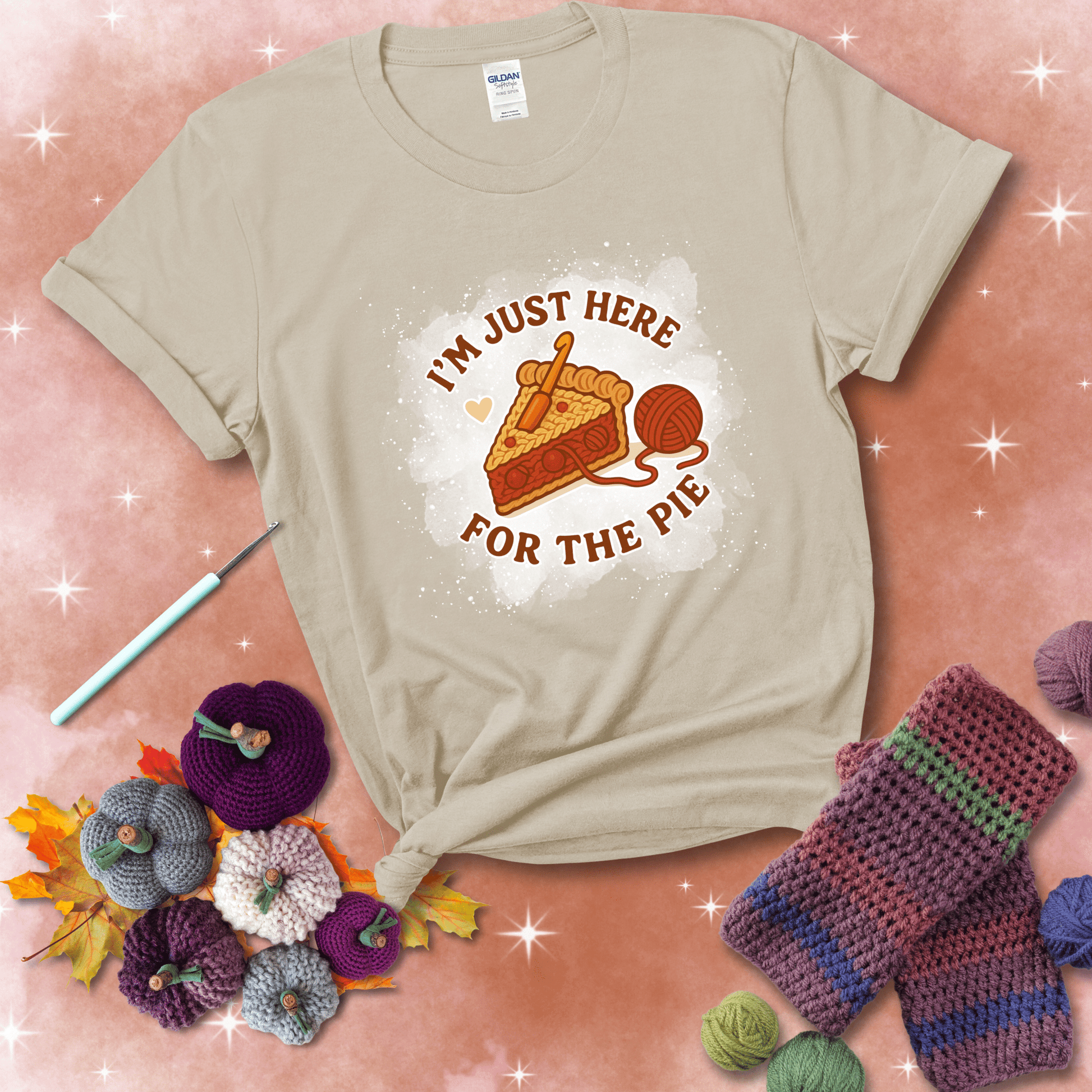 A slice of cherry pie with a crochet hook tucked in the filling and yarn trailing out, blending baking with crochet fun, showing a beige tee with a festive Fall background