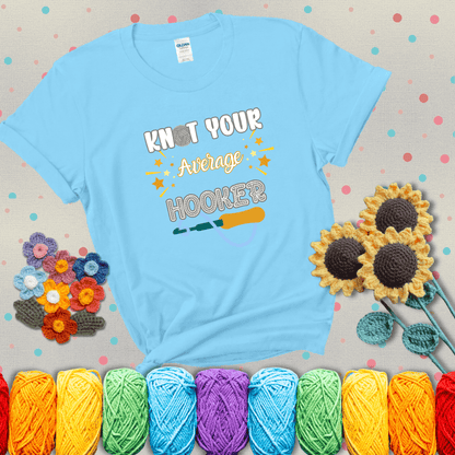 Bold lettering with a yarn hook graphic. Text reads: “I'm Not Your Average Hooker.” A cheeky crochet tee for confident crafters who own their skills, showing a light blue tee with grey sunflower background