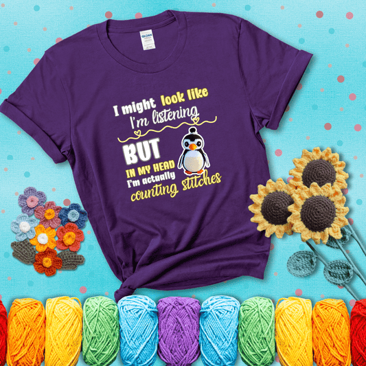 Crochet penguin next to the text “I might look like I’m listening but in my head I’m actually counting stitches” showing a purple tee with a teal sunflower background