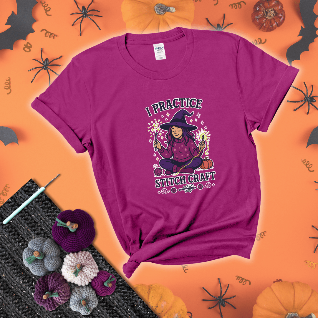 Witchy crocheter sits cross-legged, conjuring yarn magic with crochet hooks and glowing green yarn, surrounded by stars, pumpkins, and stitchy vibes showing a magenta tee with a festive Halloween background