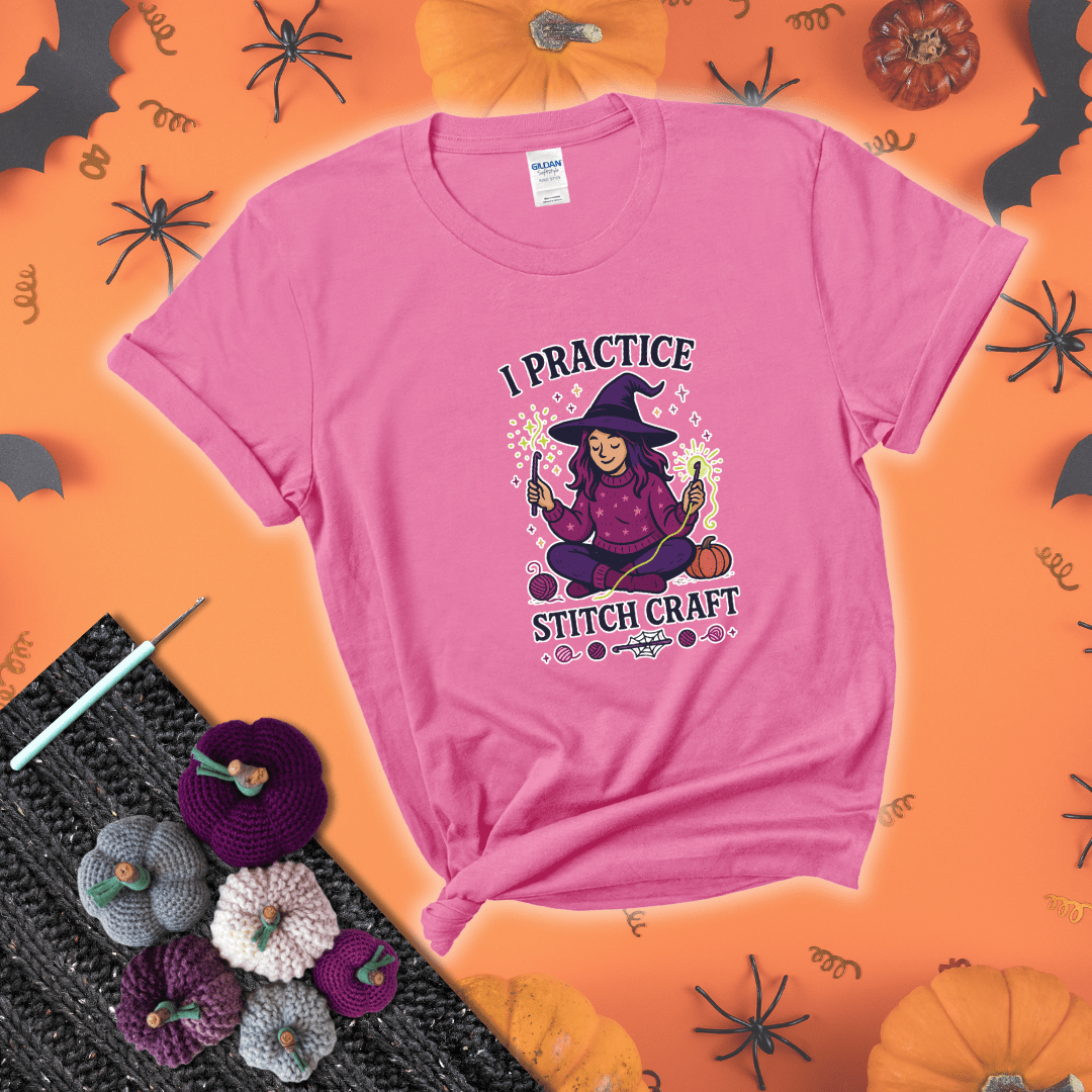 Witchy crocheter sits cross-legged, conjuring yarn magic with crochet hooks and glowing green yarn, surrounded by stars, pumpkins, and stitchy vibes showing a pink tee with a festive Halloween background
