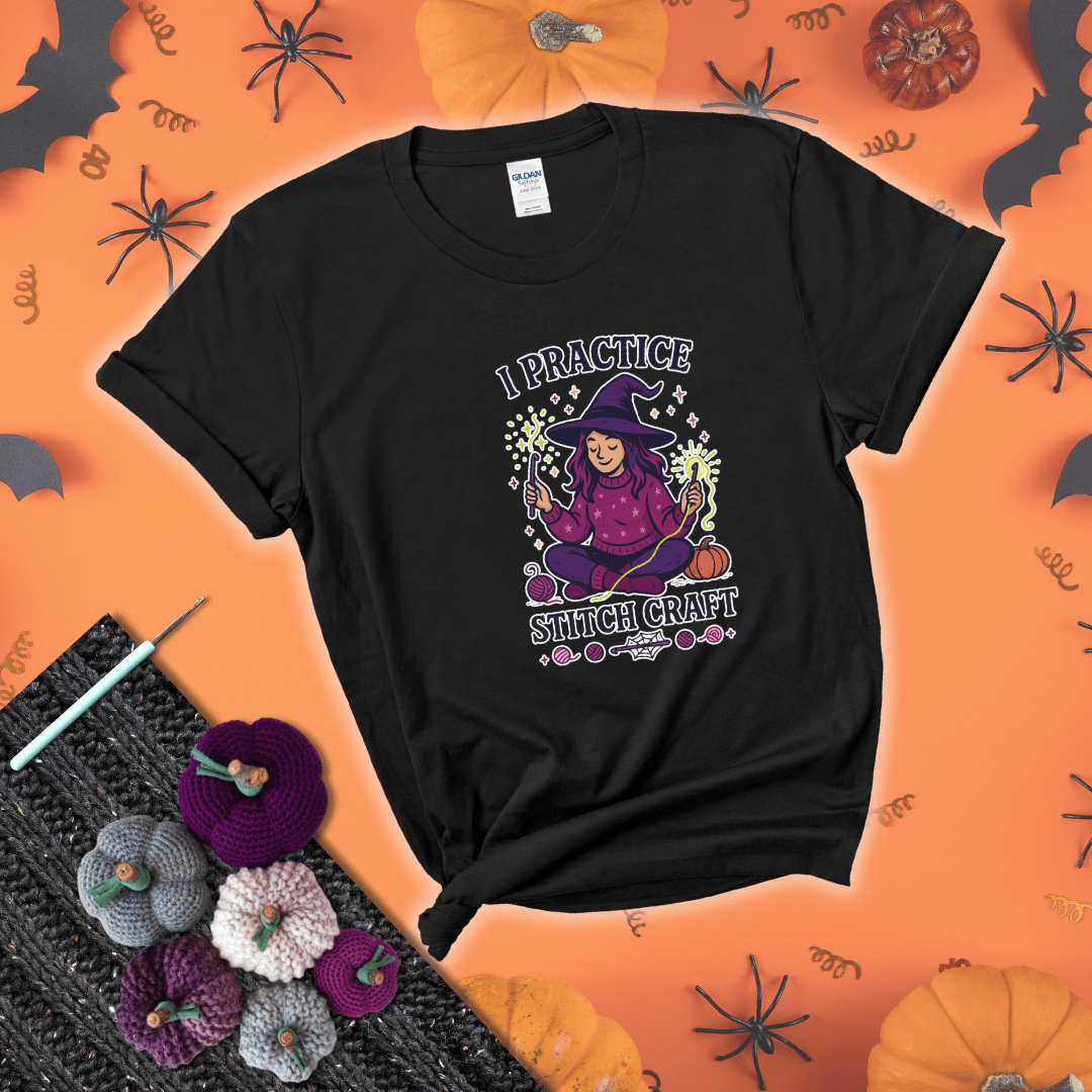 Witchy crocheter sits cross-legged, conjuring yarn magic with crochet hooks and glowing green yarn, surrounded by stars, pumpkins, and stitchy vibes showing a black tee with a festive Halloween background