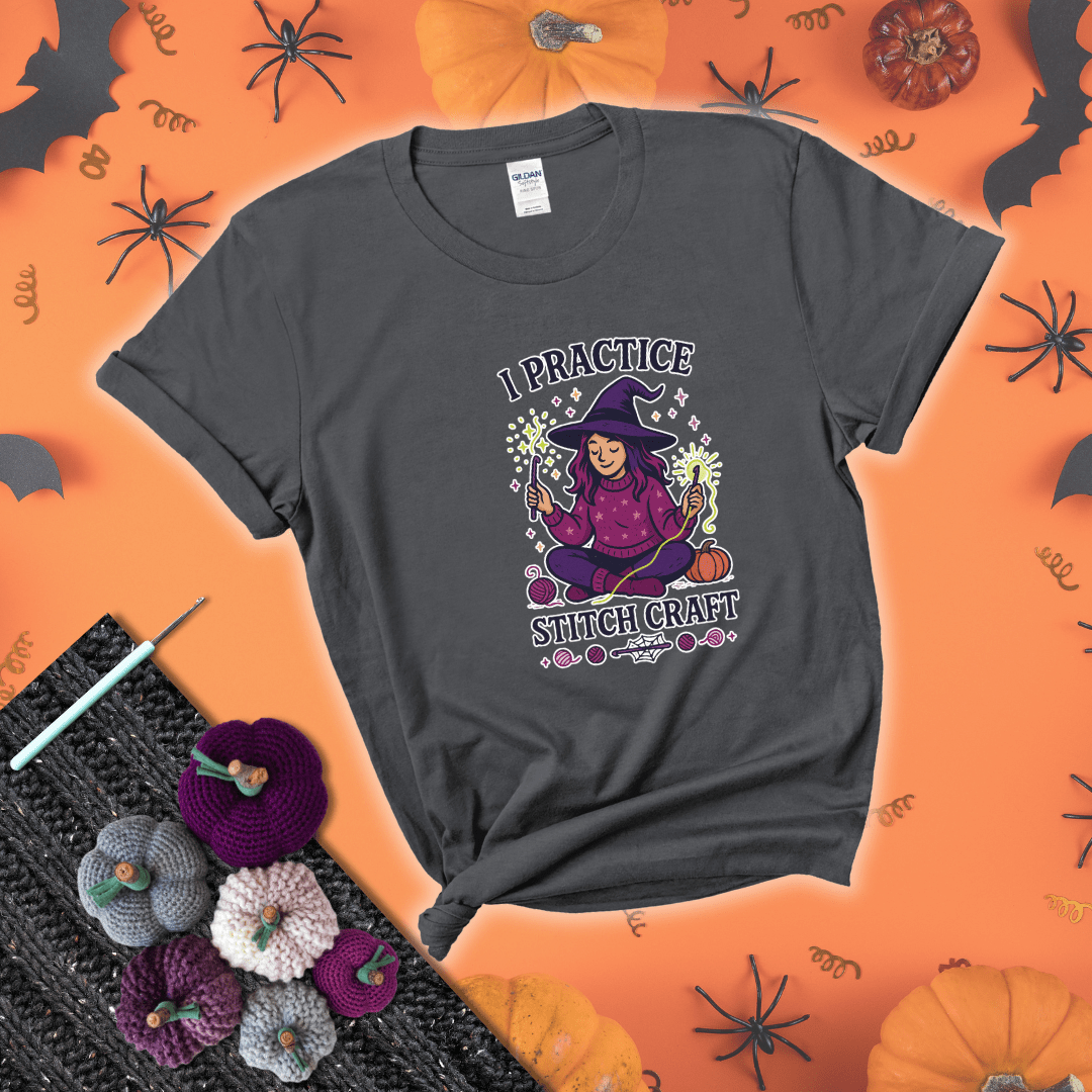Witchy crocheter sits cross-legged, conjuring yarn magic with crochet hooks and glowing green yarn, surrounded by stars, pumpkins, and stitchy vibes showing a dark grey tee with a festive Halloween background