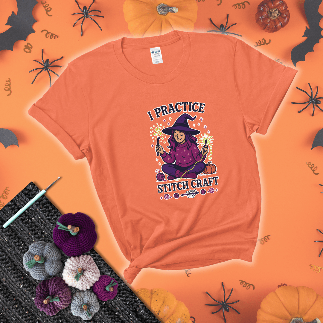 Witchy crocheter sits cross-legged, conjuring yarn magic with crochet hooks and glowing green yarn, surrounded by stars, pumpkins, and stitchy vibes showing a light orange tee with a festive Halloween background