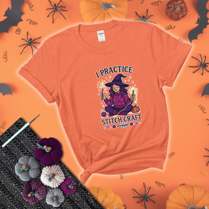 Witchy crocheter sits cross-legged, conjuring yarn magic with crochet hooks and glowing green yarn, surrounded by stars, pumpkins, and stitchy vibes showing a light orange tee with a festive Halloween background