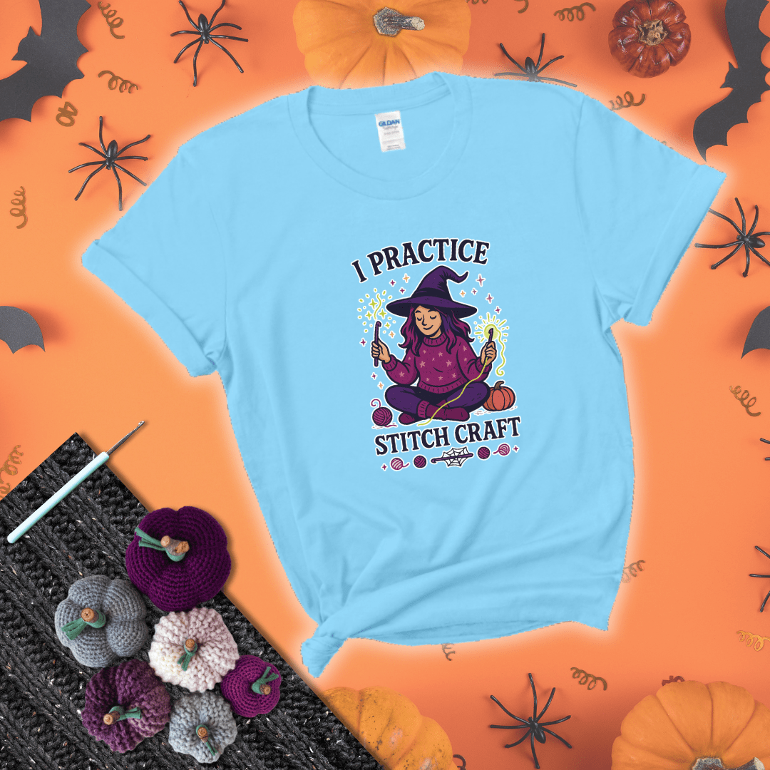 Witchy crocheter sits cross-legged, conjuring yarn magic with crochet hooks and glowing green yarn, surrounded by stars, pumpkins, and stitchy vibes showing a light blue tee with a festive Halloween background