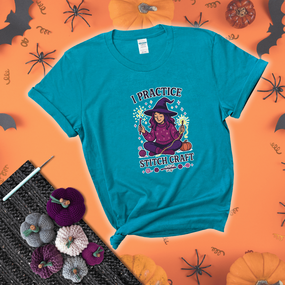 Witchy crocheter sits cross-legged, conjuring yarn magic with crochet hooks and glowing green yarn, surrounded by stars, pumpkins, and stitchy vibes showing a blue-green tee with a festive Halloween background