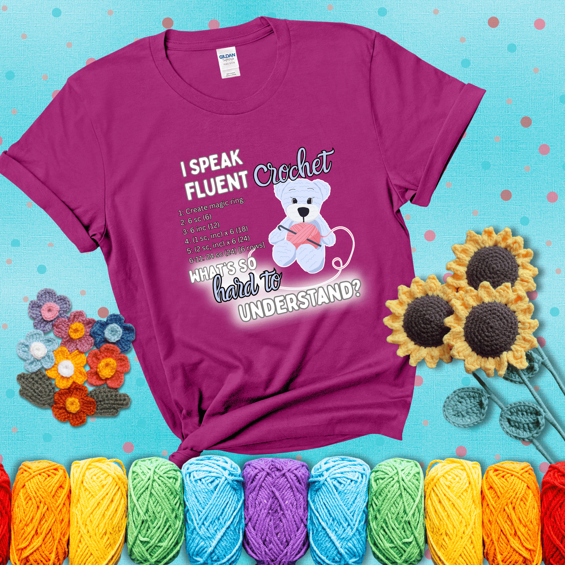 A cute crochet bear holding a yarn ball, surrounded by a short crochet pattern. The phrase reads “I Speak Fluent Crochet – What’s so hard to understand?” showing a magenta tee with a teal sunflower background
