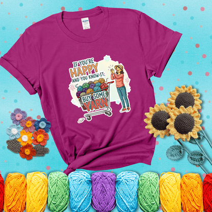 Woman clapping beside a shopping cart overflowing with colorful yarn balls, styled with cheerful pastel accents and bold playful lettering showing a magenta tee with a teal sunflower background