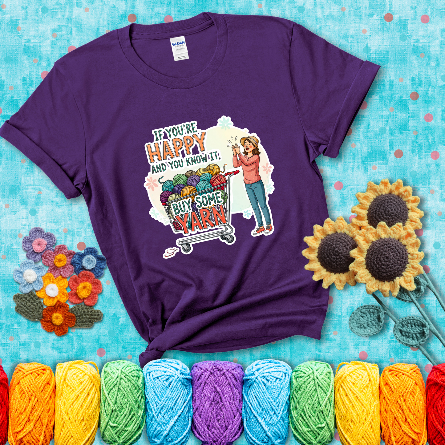 Woman clapping beside a shopping cart overflowing with colorful yarn balls, styled with cheerful pastel accents and bold playful lettering showing a purple tee with a teal sunflower background