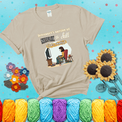 A girl with a crochet hook sits under a granny square blanket watching TV, with yarn, a coffee mug, and a cat at her feet. Text says “Introvert’s version of Netflix and chill (yes, really)," showing a beige tee with a teal sunflower background