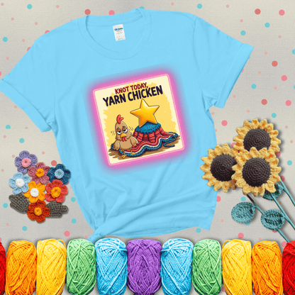 A frazzled cartoon chicken stands next to a nearly-finished project with minimal yarn left, with the phrase “Knot Today, Yarn Chicken” above, showing a light blue tee with grey sunflower background