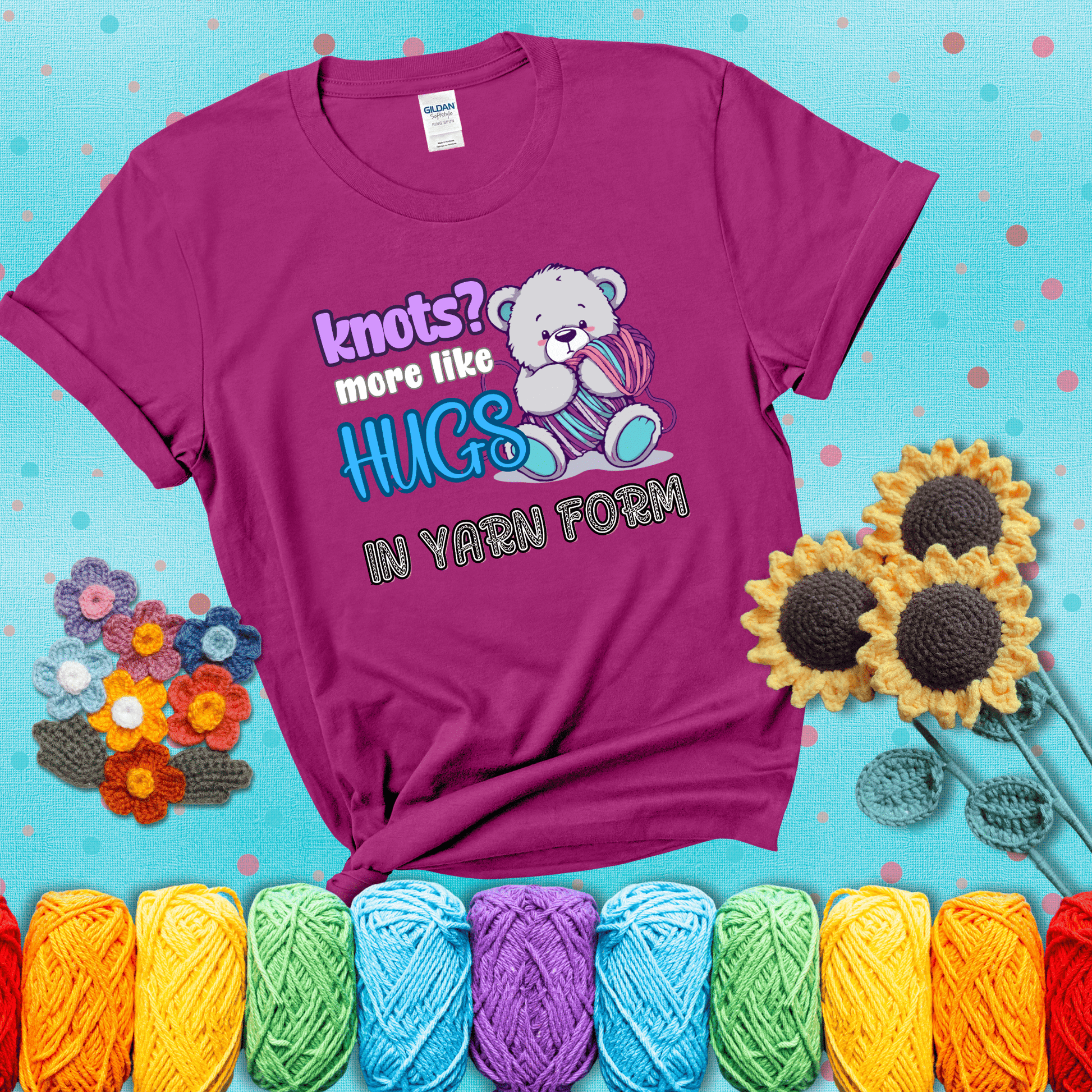 Cute teddy bear holding colorful yarn ball with hearts. Text reads: “Knots? More Like Hugs in Yarn Form.” Perfect for cozy gift-givers and yarn lovers, showing a magenta tee with a teal sunflower background