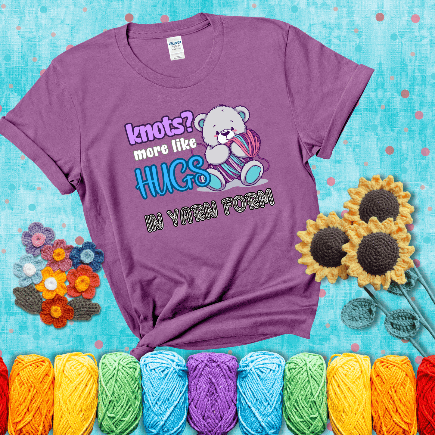 Cute teddy bear holding colorful yarn ball with hearts. Text reads: “Knots? More Like Hugs in Yarn Form.” Perfect for cozy gift-givers and yarn lovers, showing a light purple tee with a teal sunflower background