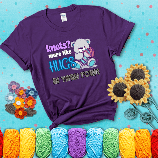 Cute teddy bear holding colorful yarn ball with hearts. Text reads: “Knots? More Like Hugs in Yarn Form.” Perfect for cozy gift-givers and yarn lovers, showing a purple tee with a teal sunflower background