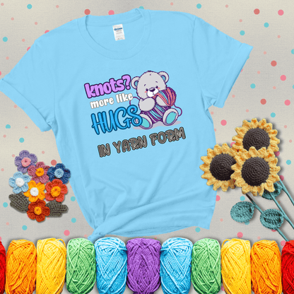 Cute teddy bear holding colorful yarn ball with hearts. Text reads: “Knots? More Like Hugs in Yarn Form.” Perfect for cozy gift-givers and yarn lovers, showing a light blue tee with grey sunflower background