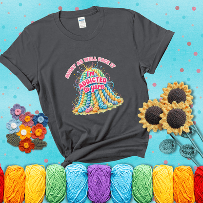 Colorful mountain of pastel yarn hanks with the phrase “Might as well face it, I’m addicted to yarn” in playful pink and red lettering showing a dark grey tee with a teal sunflower background