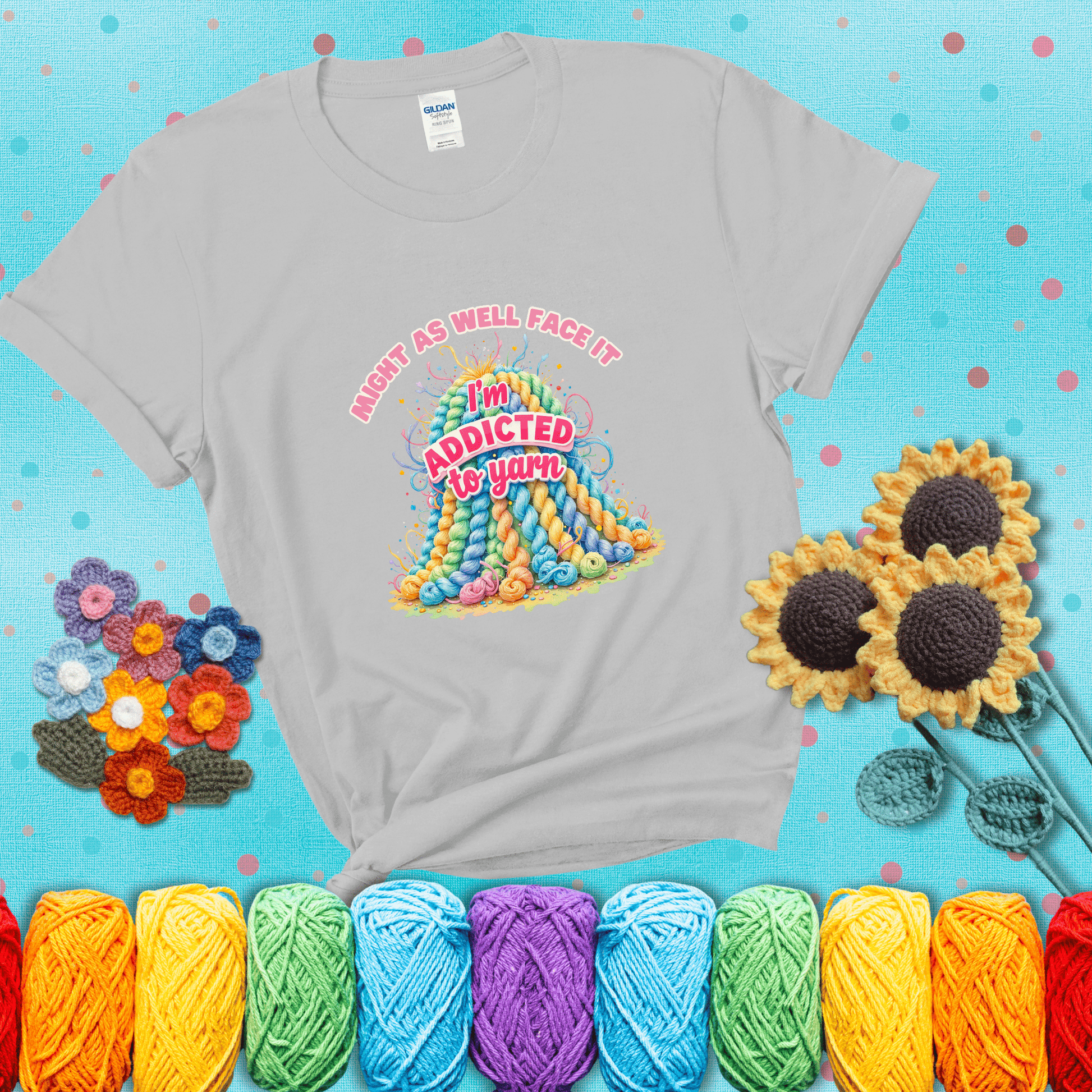 Colorful mountain of pastel yarn hanks with the phrase “Might as well face it, I’m addicted to yarn” in playful pink and red lettering showing a light grey tee with a teal sunflower background