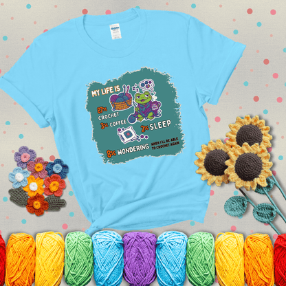 A relaxed frog crocheting while sipping coffee, surrounded by yarn and dreaming of more yarn. Includes whimsical text dividing life into percentages: 87% crochet, 3% coffee, 2% sleep, 8% wondering when to crochet again showing a light blue tee with grey sunflower background