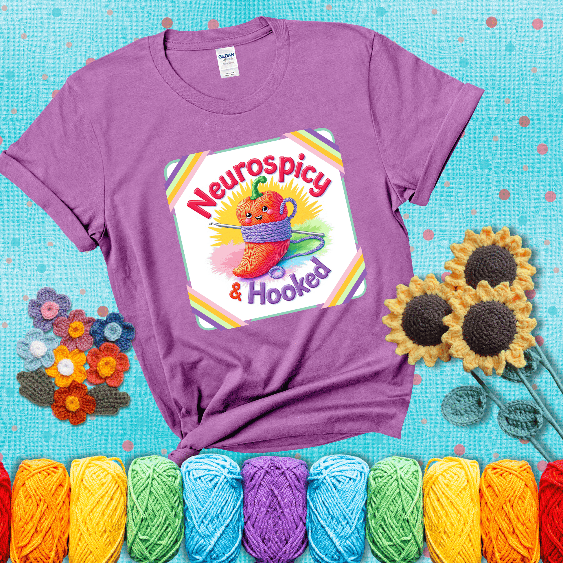 A cheerful red pepper wrapped in purple yarn with a crochet hook, framed by pastel rainbow corners and the words "Neurospicy & Hooked" showing a light purple tee with a teal sunflower background
