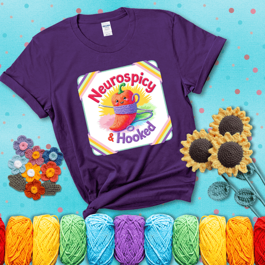 A cheerful red pepper wrapped in purple yarn with a crochet hook, framed by pastel rainbow corners and the words "Neurospicy & Hooked" showing a purple tee with a teal sunflower background
