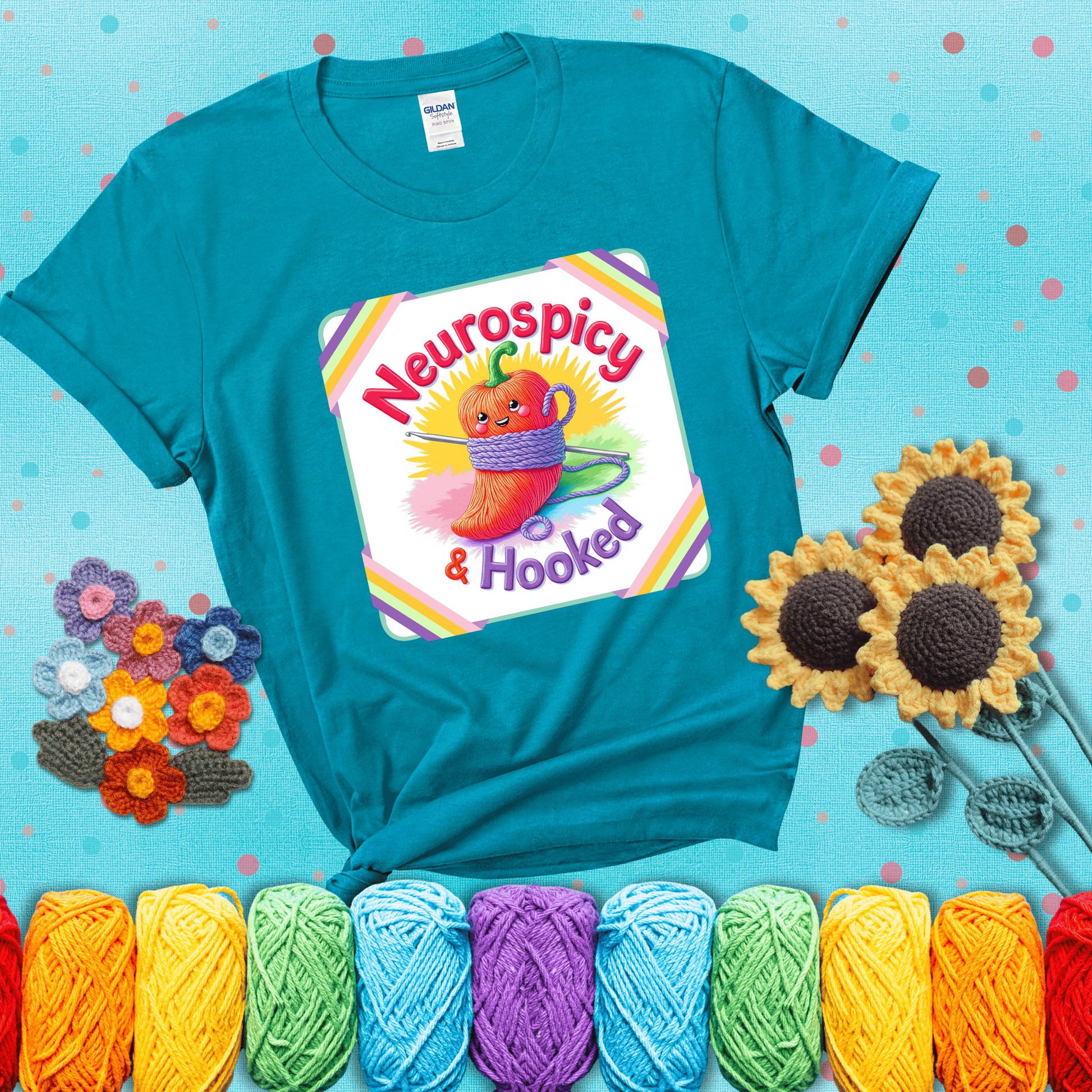 A cheerful red pepper wrapped in purple yarn with a crochet hook, framed by pastel rainbow corners and the words "Neurospicy & Hooked" showing a blue-green tee with a teal sunflower background