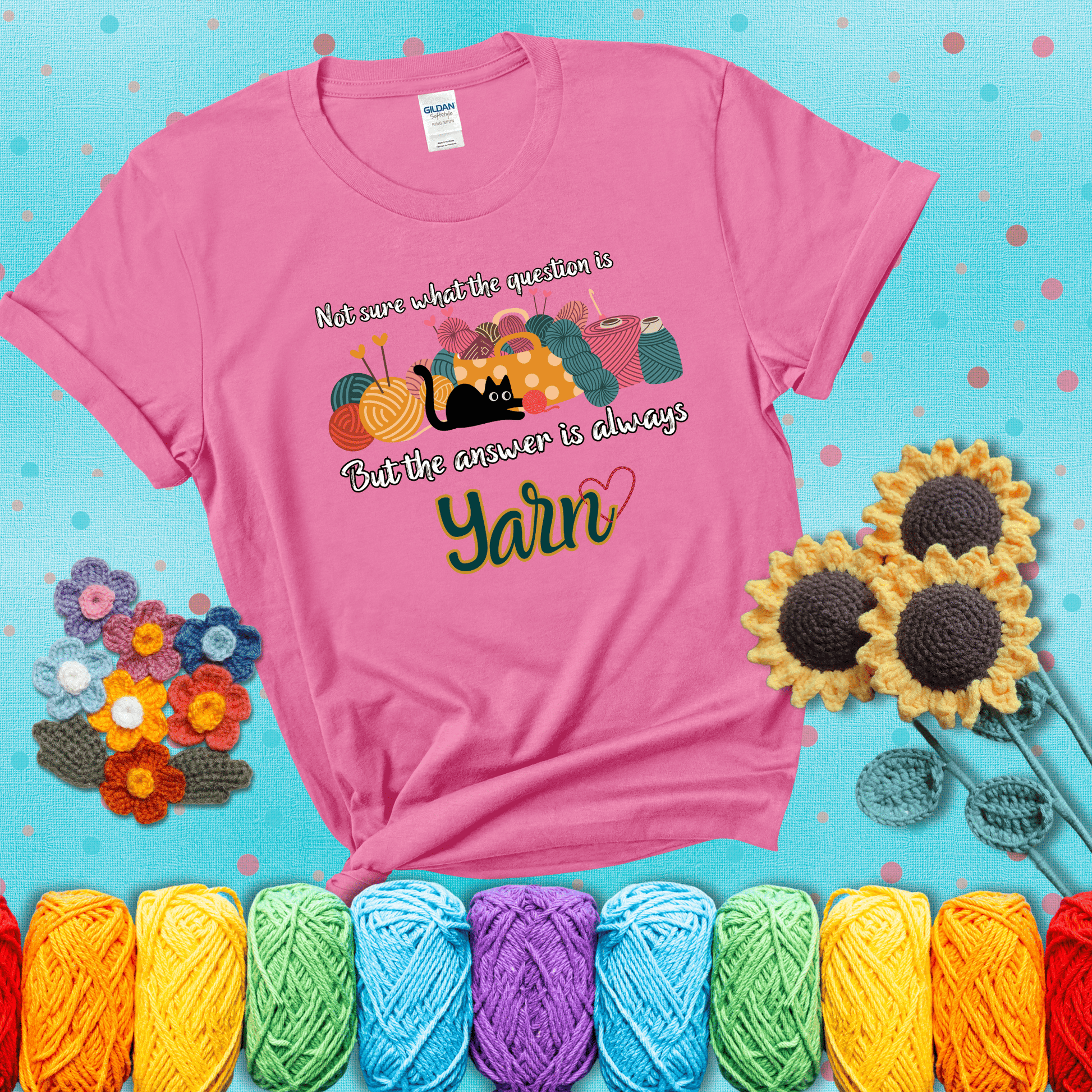 Illustration of a black cat playing with yarn next to a basket full of colorful skeins, with the phrase "Not sure what the question is, but the answer is always yarn" showing a pink tee with a teal sunflower background